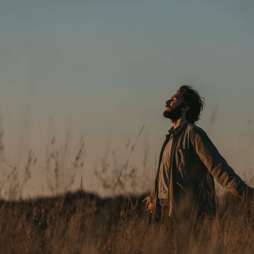 A man stands in a golden field with arms open and eyes closed, soaking in the peacefulness that comes with addiction treatment in Palm Springs.