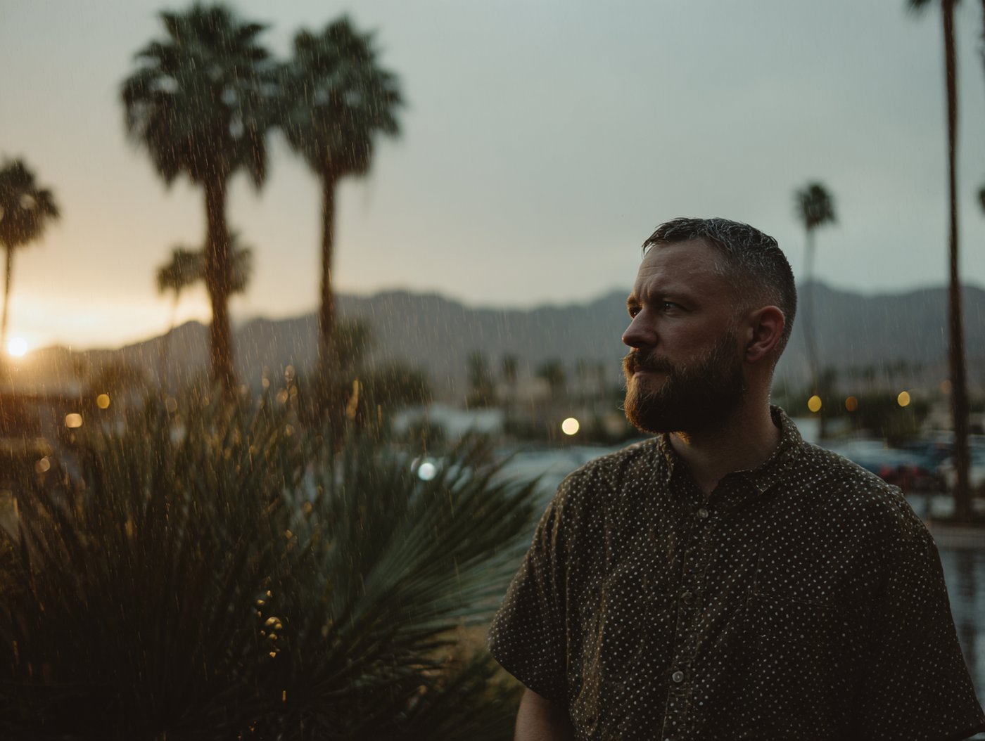A man stands in the rain at sunset among palm trees, reflecting the resilience and depth behind solutionpoint beliefs and ethics.