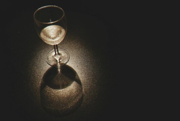 An empty wine glass on a dark table illuminated by light, representing the effects of Ethanol Addiction.