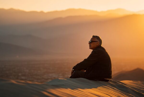 A man sitting on desert sand dunes at sunset, symbolizing reflection and the risks of mixing Ativan with other substances.