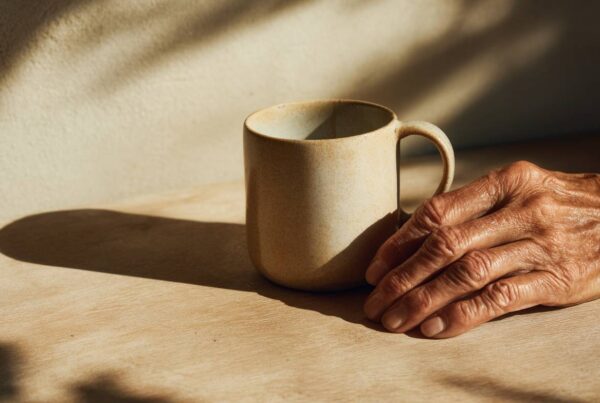 An older adult’s hand rests beside a ceramic mug in warm morning light, reflecting the quiet need for alcohol addiction help for older adults.
