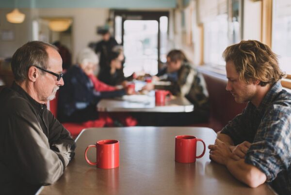 A father and adult son sitting quietly across from each other in a diner, reflecting the heavy concern behind the words my son is addicted.